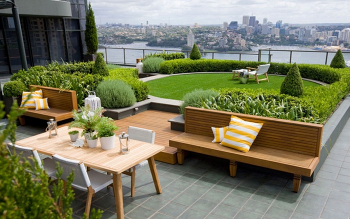 hình ảnh toàn cảnh sân vườn trên sân thượng với thảm cỏ xanh mướt, cây cảnh cắt tỉa gọn gàng, bàn ghế gỗ thư giãn, lan can kính cường lực trong suốt