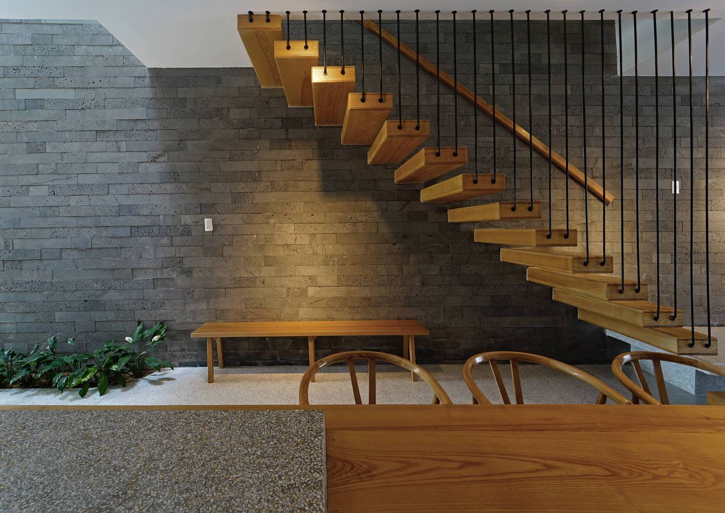hình ảnh khu vực cầu thang gỗ bậc hở trong nhà đẹp, cây xanh, tường ốp đá bê tông xám, bàn ăn gỗ đặt bên cạnh