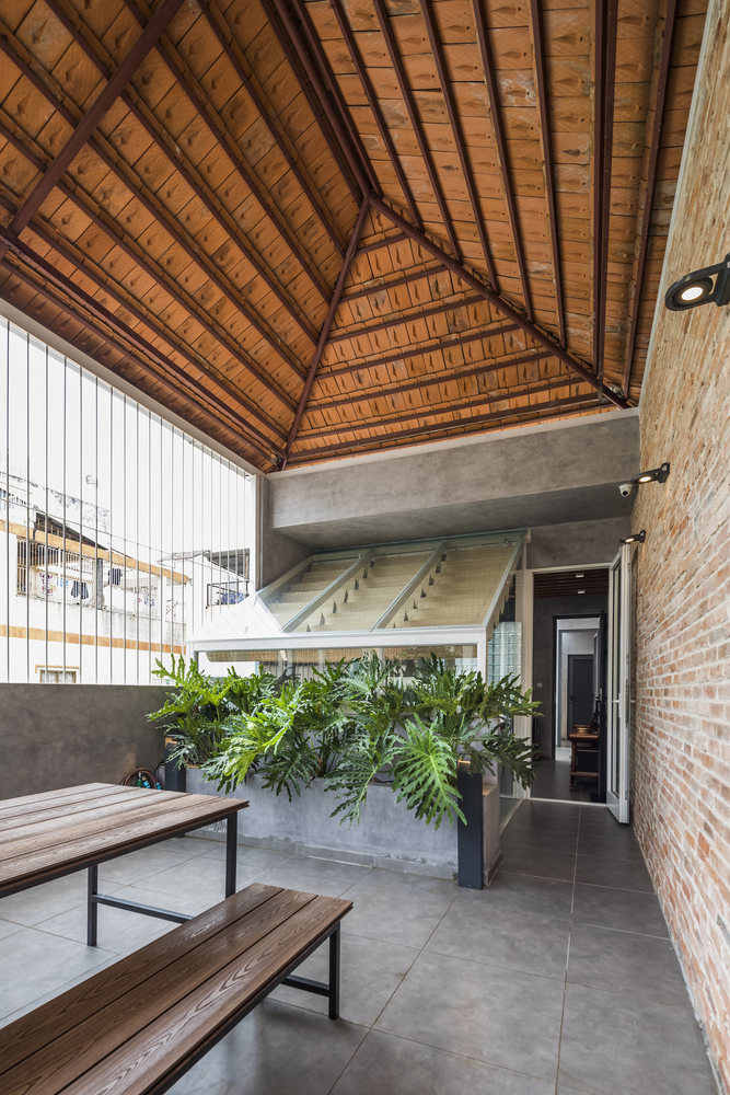 không gian bên trong nhà Sài Gòn với mái lợp ngói, dầm thép, bàn ghế gỗ, bồn cây xanh tốt