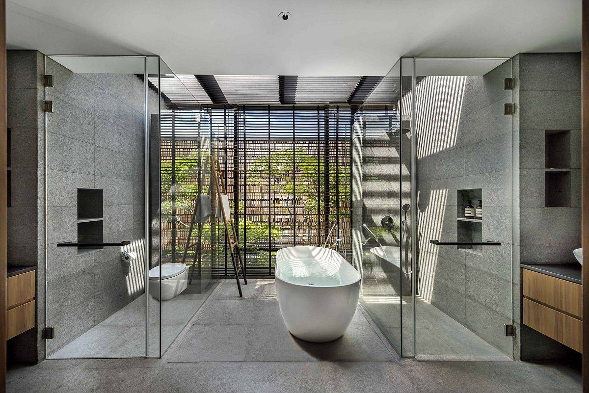 Phòng tắm phong cách đương đại với tường và sàn bê tông xám thanh lịch, tường kính trong suốt và bồn tắm sứ trắng hiện đại, sang trọng.