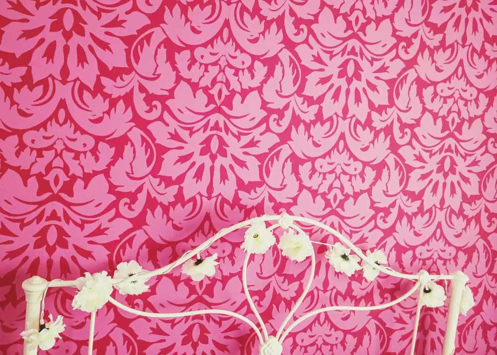 cận cảnh đầu giường bằng kim loại sơn trắng, uốn lượn kiểu cách, giấy dán tường màu hồng đỏ họa tiết phức tạp