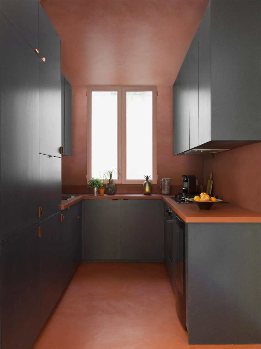 Bếp hình chữ U gọn gàng, tiện nghi với hệ tủ màu xám đen kết hợp hài hòa với màu đỏ gạch của sàn và tường, bề mặt bàn bếp.