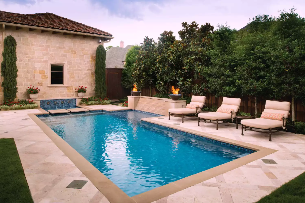 Bể bơi hình chữ nhật phù hợp với khuôn viên sân sau có diện tích vừa phải. Sàn xung quanh hồ bơi bằng bê tông, lát gạch giả đá cùng tông với ngôi nhà.