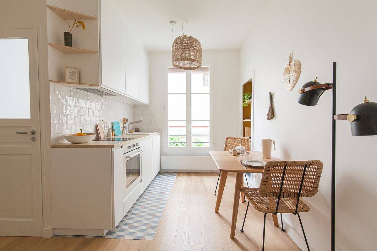 Nhà bếp nhỏ phong cách Scandinavian với tông màu trắng ngà chủ đạo. Bàn ăn bằng gỗ, ghế mây mộc mạc tạo điểm nhấn ấm áp.