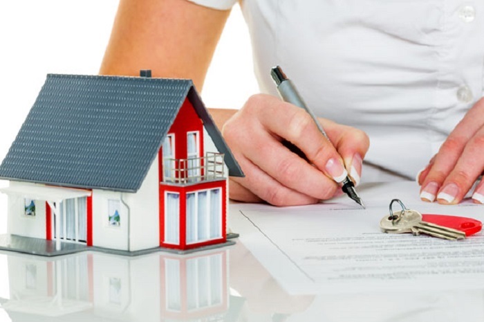 hình ảnh một người đang ký hợp đồng mua nhà, bên cạnh là mô hình ngôi nhà