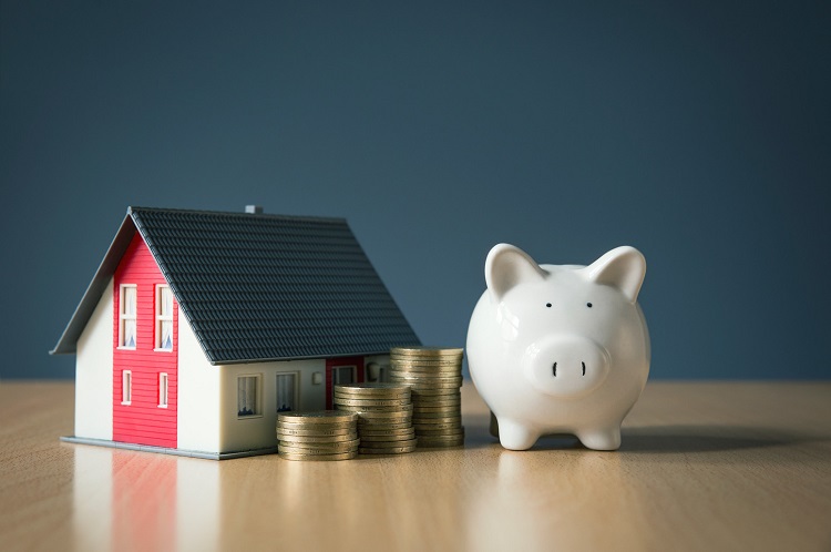 hình ảnh mô hình ngôi nhà, các cọc tiền xu và chú lợn tiết kiệm màu trắng ngà minh họa cho việc vay mua nhà đất