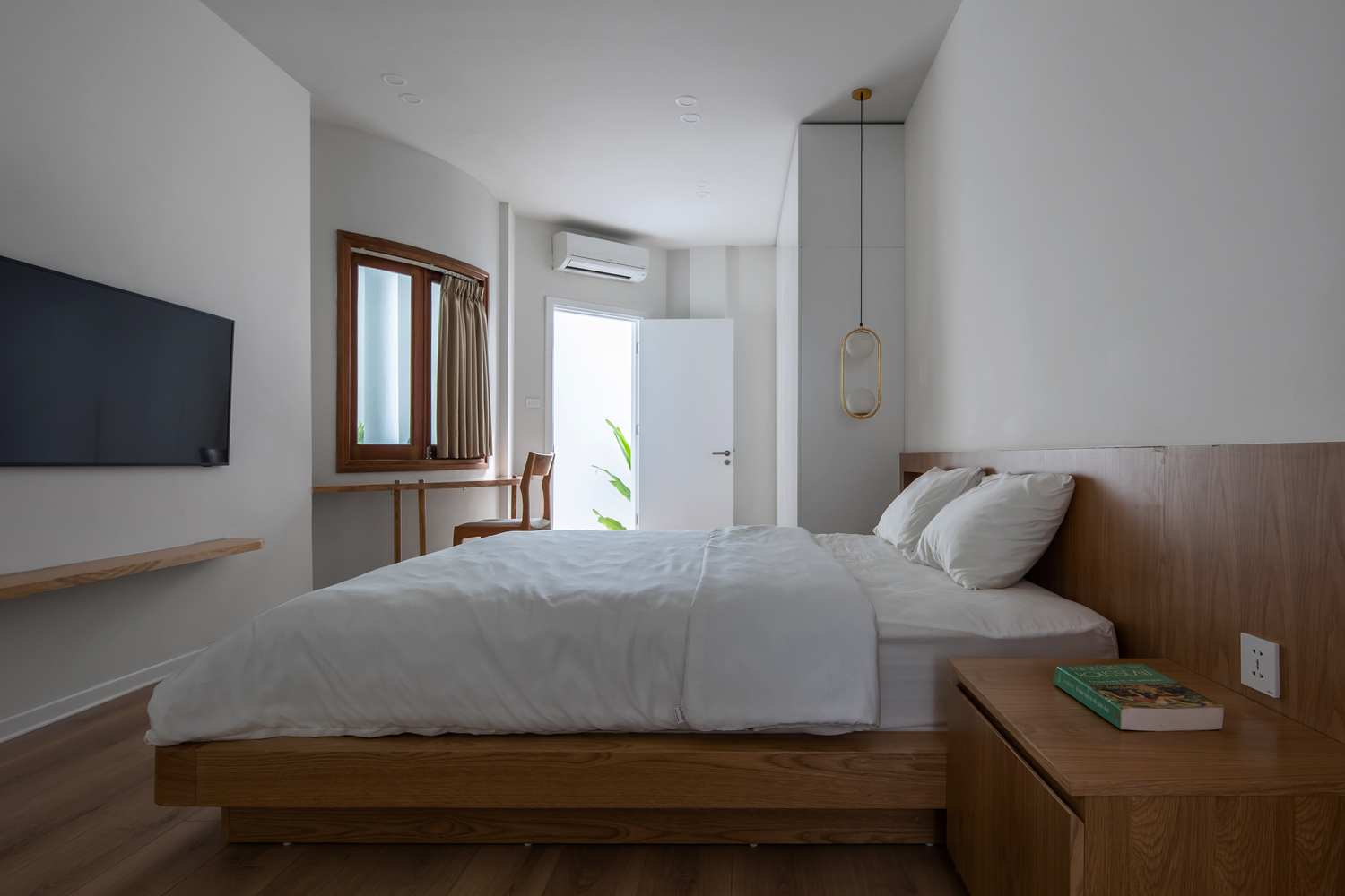 phòng ngủ với giường gỗ nệm trắng, tivi treo tường