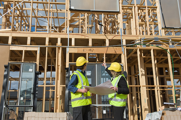 hình ảnh hai kỹ sư cầm bàn vẽ đứng cạnh ngôi nhà đang trong quá trình xây dựng minh họa cho thuế xây dựng nhà ở.