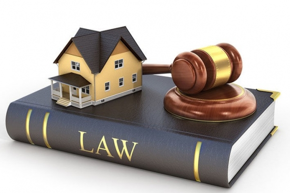 hình ảnh mô hình ngôi nhà và búa pháp luật đặt trên cuốn sách dày, gáy sách in chữ LAW