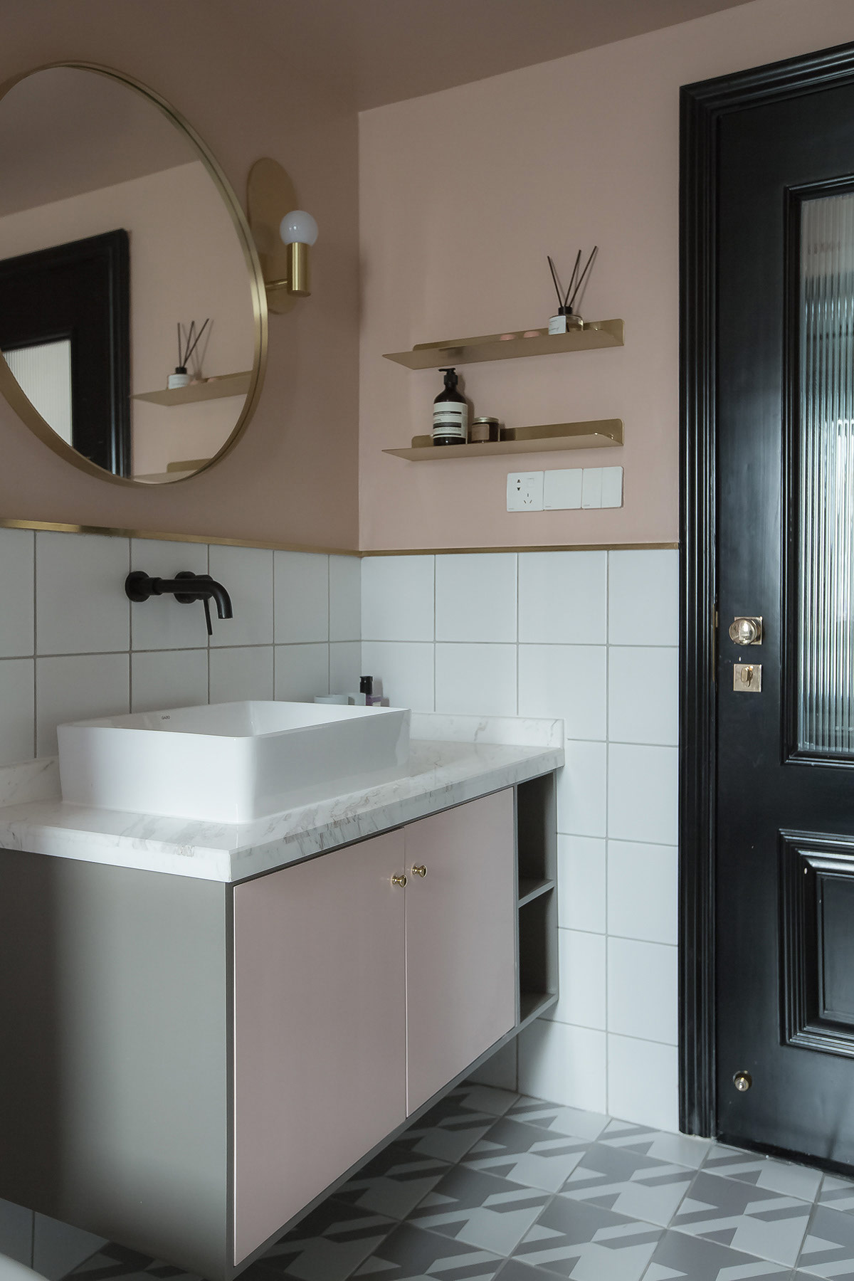 Gương tròn lớn với khung vàng kim loại và đèn treo tường phòng tắm tạo thành một bộ đôi quyến rũ phía trên bồn rửa.