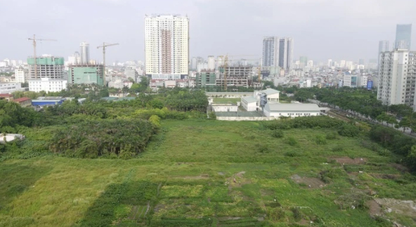 Hình ảnh khu đất trống cỏ mọc xanh tốt cạnh các tòa nhà cao tầng, đô thị minh họa cho việc thu hồi đất