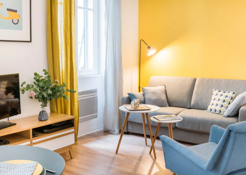 Rèm cửa và bức tường điểm nhấn tông màu vàng bơ mang lại nhiều năng lượng dương cho phòng khách căn hộ Studio