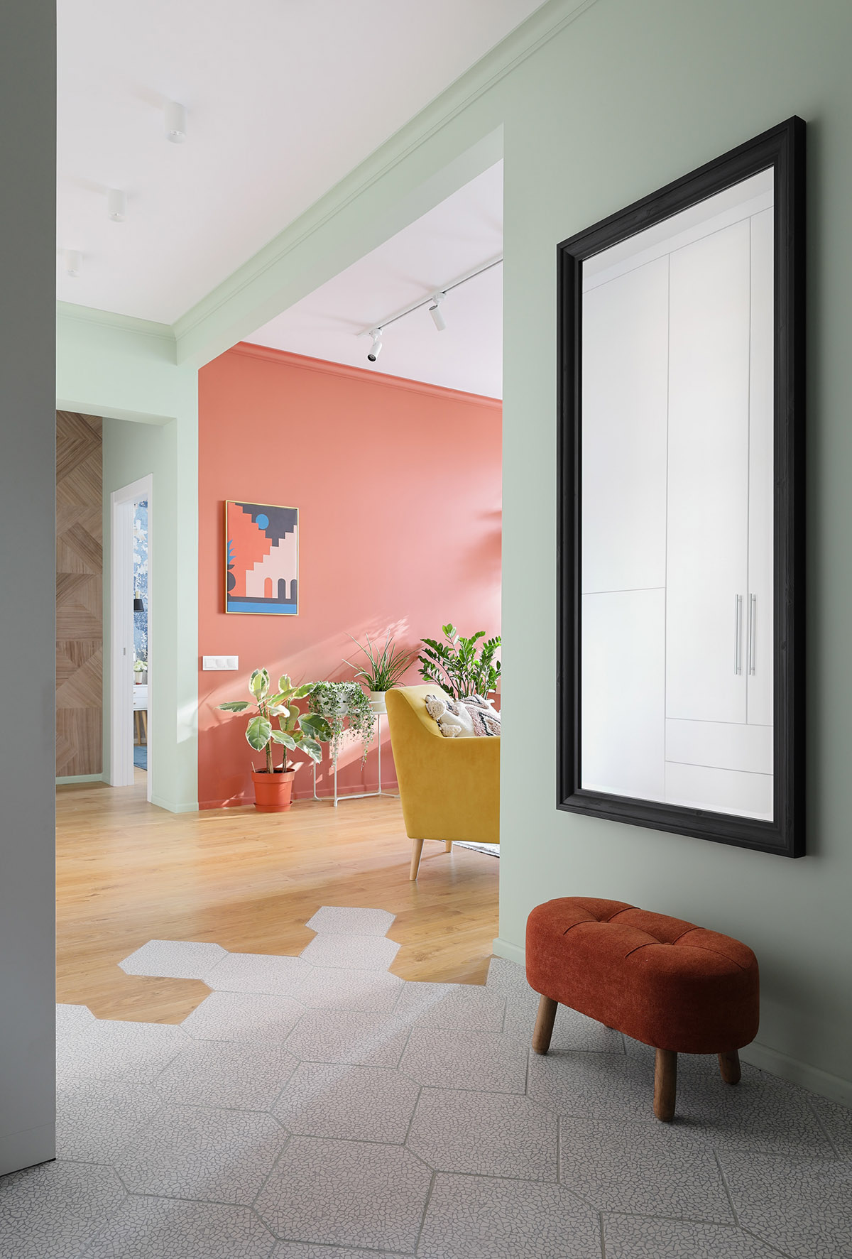 Bức tường điểm nhấn màu cam san hô làm nền cho sắc xanh thiên nhiên thêm phần nổi bật. Ở lối vào căn hộ, một băng ghế nhỏ lặp lại màu san hô tạo sự liền mạch.
