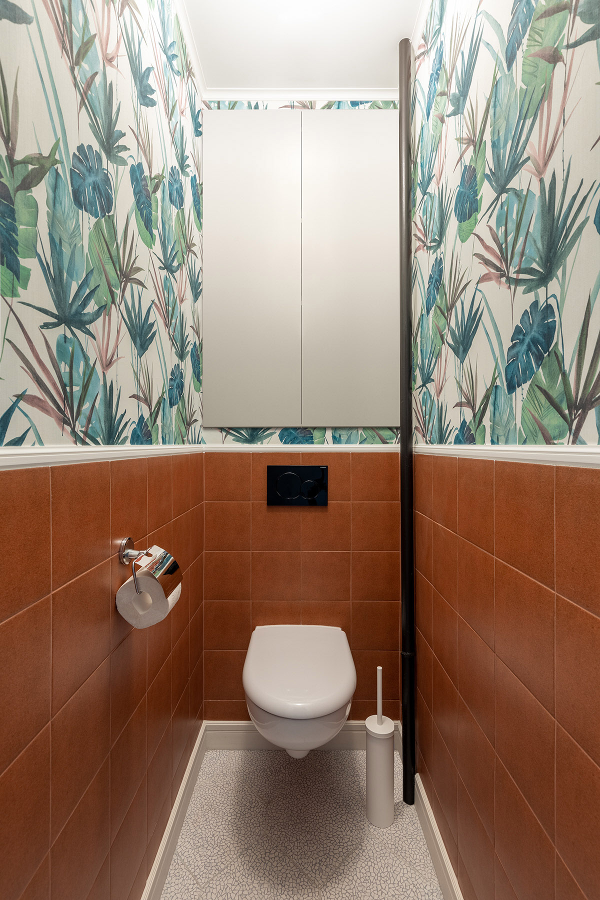 WC nhỏ xinh với gạch ốp tông màu đất thân thiện, phần tường phía trên trang trí giấy dán tường họa tiết nhiệt đới xanh mát.