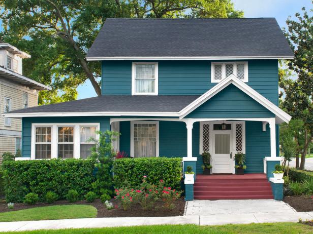 hình ảnh ngôi nhà với tường sơn màu xanh hải quân, mái màu xám, bậc thềm sơn đỏ nằm dưới tán cây lớn