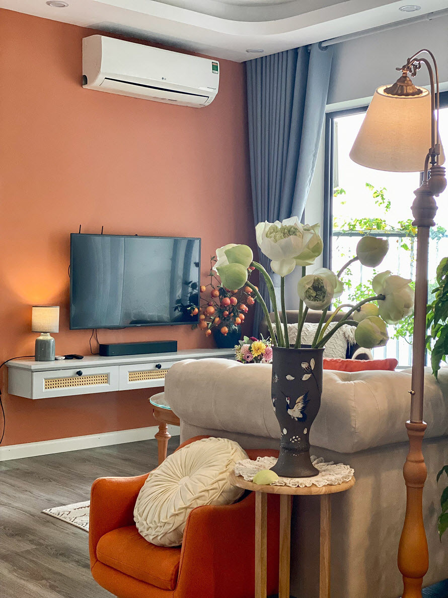 Góc phòng khách với tường sau tivi sơn màu cam, ghế bành màu cam, bình hoa sen 
