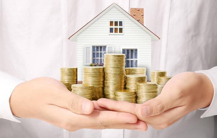 hình ảnh một người mặc sơ mi trắng ôm mô hình ngôi nhà và các cọc tiền xu minh họa cho việc bán nhà chung cư