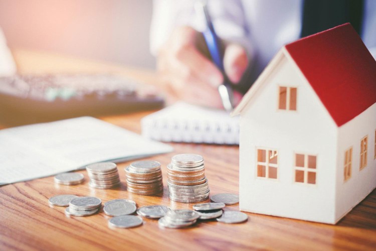 mô hình ngôi nhà mái đỏ cạnh các cọc tiền xu trên bàn minh họa cho tín dụng bất động sản